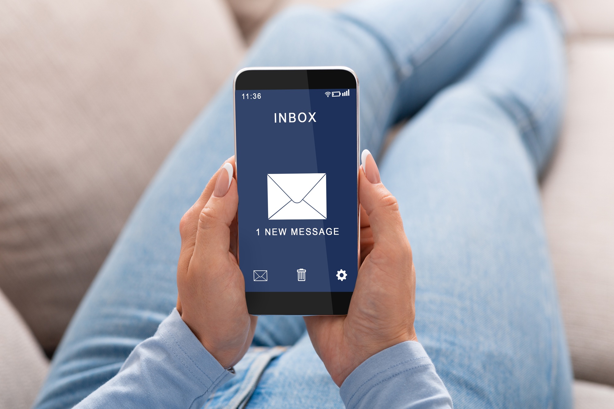 Woman Reading E-Mail Message On Smartphone Sitting On Couch Indoor
